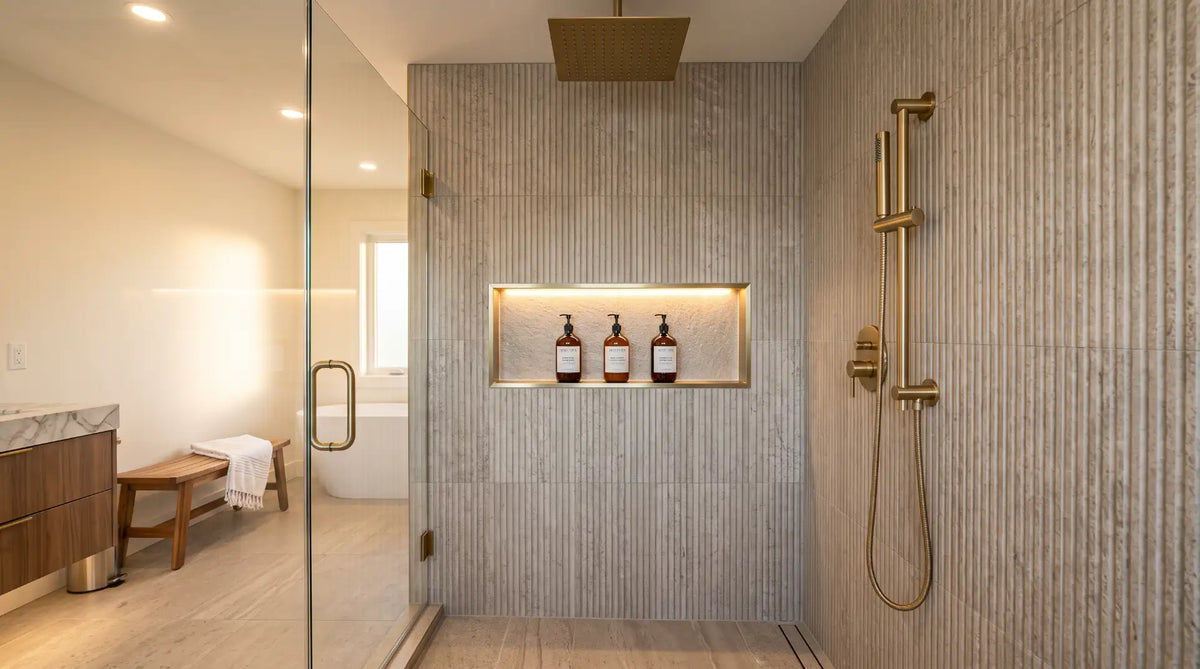 Modern tiled shower interior featuring a brushed gold recessed storage niche and a matching hand shower kit in a Canadian home.